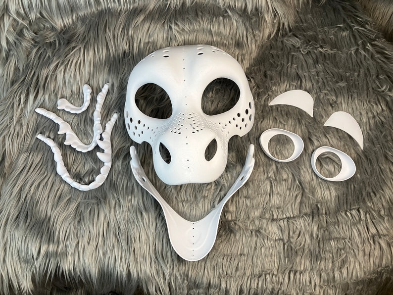 May include: White unfinished plastic mask with separate pieces for eyes, nose, and teeth. The mask is designed to look like a dragon or other fantasy creature.