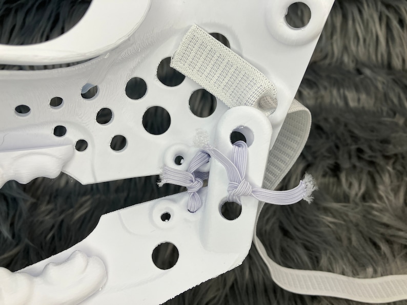 May include: White plastic helmet with a white elastic strap and a white velcro strap. The helmet has a series of holes in the plastic.