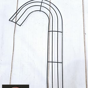 Może przedstawiać: Forma wieńca z czarnego metalowego drutu w kształcie cukierka. Forma ma kształt cukierka i ma metalową ramę z wieloma poziomymi prętami.