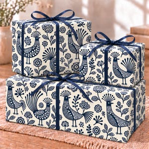 May include: Three rectangular gift boxes wrapped in cream-colored paper featuring a repeating dark blue pattern of stylized birds and flowers. Each box is tied with a dark blue satin ribbon bow centered on the top surface of the package.