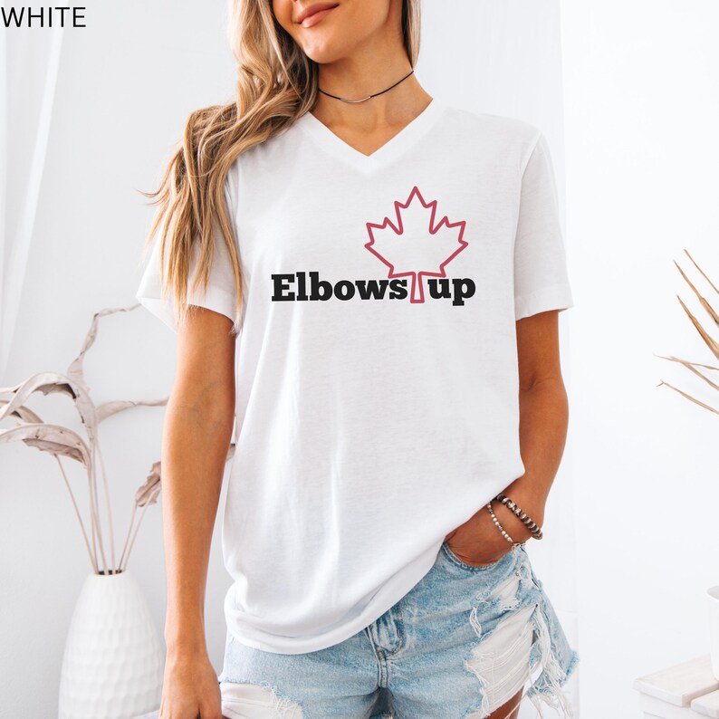 May include: White V-neck t-shirt with a red outline of a Canadian maple leaf and the text "Elbows Up" in black.