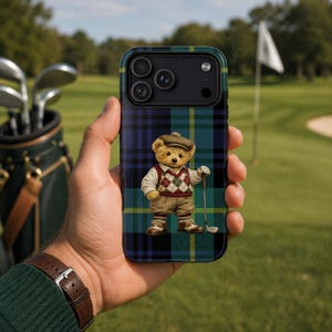 May include: A smartphone case with a plaid pattern in shades of blue, green, and yellow. The case features a cartoon teddy bear dressed in golf attire, holding a golf club. The background shows a golf course.