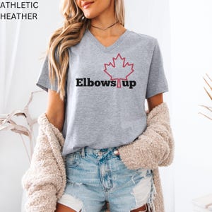 May include: A grey V-neck t-shirt with a red outline of a Canadian maple leaf and the text "Elbows Up" in black.