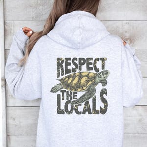 May include: A grey hoodie with a graphic of a sea turtle and the text "Respect the Locals" printed on the back.
