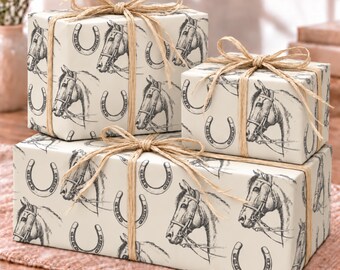 May include: Three rectangular gift boxes wrapped in cream-colored paper featuring a repeating black ink sketch pattern of horse heads and horseshoes. Each box is tied with a natural tan raffia ribbon tied in a bow on the top center.