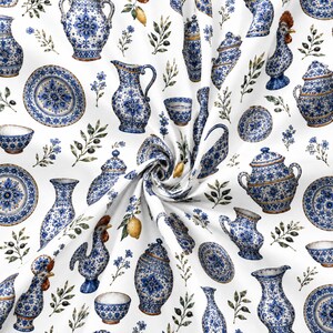 May include: A white fabric featuring a repeating pattern of blue and white ceramic pottery, including pitchers, lidded jars, bowls, and plates, interspersed with illustrations of yellow lemons, green olive branches, and small blue flowers.