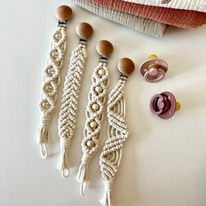 May include: Four handmade macrame baby teethers with wooden beads and clips. The teethers are in a variety of patterns and are a light cream color.