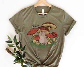 Puede incluir: Una camiseta verde con un gráfico de un gato sentado debajo de un hongo con el texto "find me".