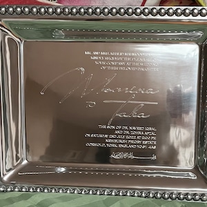 May include: Silver serving tray with a beaded border and engraved text. The text reads: "Mr. and Mrs. Khaliq Mahmood request the pleasure of your company at the wedding of their beloved daughter,  Alvina to Taha, the son of Dr. Naveed Iqbal and Dr. Zohra Afzal on Saturday 2nd July 2022 at 2:00 PM, Newburgh Priory Estate, Coxwold, York, England YO81 4A8."