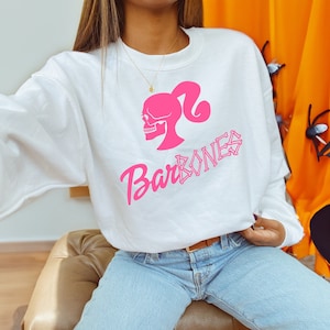 Op de afbeelding: Wit sweatshirt met een roze schedel en gekruiste botten afbeelding met de tekst "Bar Bones".