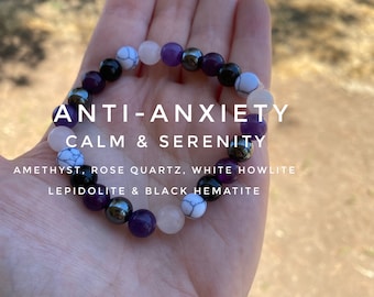 May include: A bracelet made with amethyst, rose quartz, white howlite, lepidolite, and black hematite beads. The bracelet is labeled "ANTI-ANXIETY CALM & SERENITY".