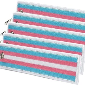 Paquete de 5 llaveros bordados con la bandera del orgullo trans en azul, blanco y rosa.