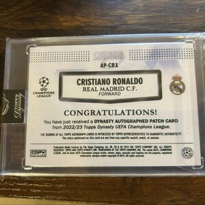 May include: A Topps Dynasty trading card featuring Cristiano Ronaldo, Real Madrid C.F. Forward. The card is in a protective case and includes the text "CONGRATULATIONS!" and "UEFA Champions League".