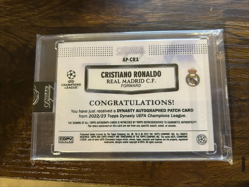 May include: A Topps Dynasty trading card featuring Cristiano Ronaldo, Real Madrid C.F. Forward. The card is in a protective case and includes the text "CONGRATULATIONS!" and "UEFA Champions League".