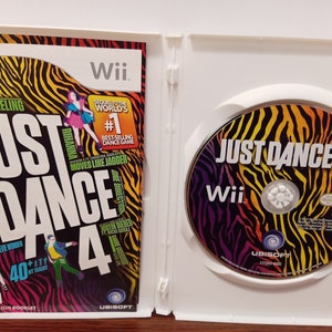 May include: Opened Wii game case for Just Dance 4. The cover features the game title in large white letters, with colorful graphics and artist names. The disc inside has the game title and Wii logo.