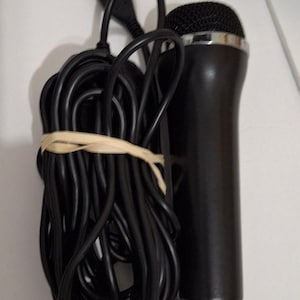 May include: A black USB microphone with a silver rim around the mesh head. The microphone has a black cable that is coiled and secured with a rubber band. The USB connector is visible.