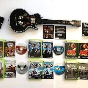 May include: A collection of video games for the Xbox 360 console, including Guitar Hero, Rock Band, and The Beatles: Rock Band. The games are displayed on a table with a black electric guitar controller.