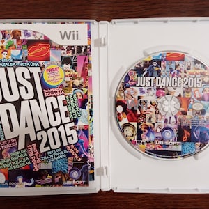 May include: Opened Wii game case for "Just Dance 2015." The cover art features a collage of images and the game title. The disc inside also displays the game title and a collage of images. The case is white.