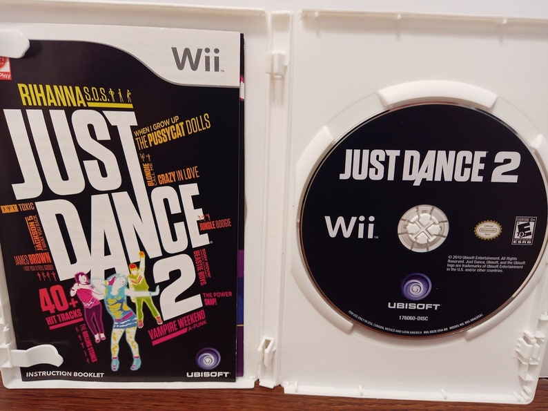 May include: A Wii game case for "Just Dance 2" featuring the game disc and instruction booklet. The booklet lists 40+ hit tracks, including songs by Rihanna, James Brown, and The Pussycat Dolls. The disc has the game title and Wii logo.