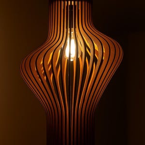 May include: A wooden pendant light with a distinctive layered design. The light is made of thin, curved wooden slats, producing a warm glow. The text "SVG-DXF-AI-DWG-PDF" and "3MM THICKNESS LASER CUTTING" are visible.