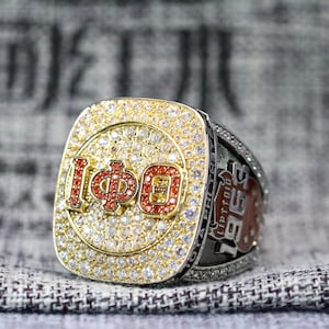 May include: A gold championship ring with a red and white logo that says "IΦD" and "1958" on the side. The ring is set with diamonds.