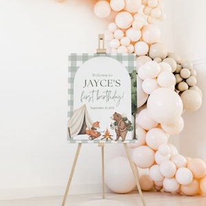 May include: A green and white checkered welcome sign with a woodland theme. The sign says "Welcome to Jayce's first birthday! September 22, 2023". The sign features a fox and a bear sitting by a campfire.