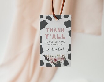 May include: A white and black cow print thank you tag with pink text that says "Thank Y'all" and "For celebrating with me at my first rodeo!" with a floral design at the bottom.