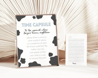 May include: A white and black cow print sign with the text "TIME CAPSULE to be opened when Jayce turns eighteen" and instructions to write a memory, advice, or prediction for the future. The sign is on a white surface with a white card with lines for writing and the word "Love" at the bottom.