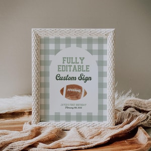 Op de afbeelding: Een wit frame met een groen-wit geruite achtergrond. De tekst "FULLY EDITABLE Custom Sign" staat in groene tekst. Een bruine voetbal bevindt zich in het midden van het bord. De tekst "JAYCE'S FIRST BIRTHDAY February 9th, 2025" staat onderaan het bord.