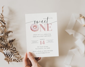 May include: A pink and white donut with sprinkles is featured on a white invitation card with the text "sweet ONE" in black and pink lettering. The invitation is for a first birthday party and includes the date, time, and location.