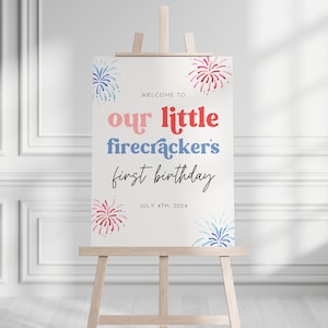 May include: Welcome to our little firecracker's first birthday sign with a white background and red, blue, and pink watercolor fireworks. The text is in a red, pink, and blue font. The date is July 4th, 2024.