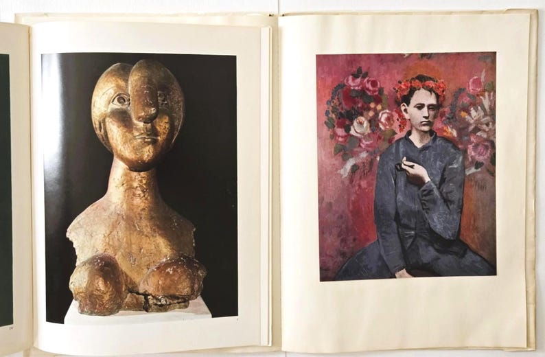 May include: An open book displaying two distinct art prints. The left page features a golden-toned, abstract bust sculpture against a black background. The right page shows a painting of a person wearing a red floral crown against a pink floral backdrop.