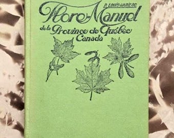 Op de afbeelding: Een lichtgroen hardcover boek met de titel Flore-Manuel de la Province de Québec Canada door P. Louis-Marie OC. De kaft bevat zwarte inktillustraties van drie esdoornbladeren en esdoornzaden op de voorzijde.