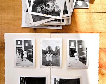 Op de afbeelding: Een verzameling vintage zwart-witfoto's, waarvan sommige op een witte albumpagina zijn geplakt en andere op een stapel liggen. De foto's tonen diverse buitenscènes, gebouwen en mensen, met handgeschreven data zoals AUG 1942 en MAR 1939.