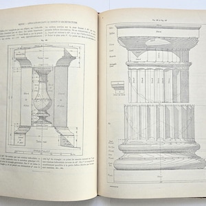 Peut inclure: Livre ouvert présentant des dessins d'architecture. La page de gauche montre un diagramme détaillé d'une colonne avec des mesures et des annotations. La page de droite présente une conception de colonne différente, également avec des dessins techniques. La couverture du livre est sombre avec un motif marbré.