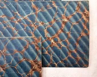 Op de afbeelding: Drie rechthoekige vellen papier met een gemarmerd ontwerp. Het papier heeft een blauwe achtergrond met bruine en witte adering. Het patroon doet denken aan natuursteen of water.