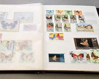 Op de afbeelding: Een postzegelalbum open op twee pagina's met een verzameling postzegels die verschillende vlindersoorten afbeelden. De linkerpagina is bedekt met een doorschijnend beschermvel, terwijl de rechterpagina rijen kleurrijke vlinderpostzegels toont.