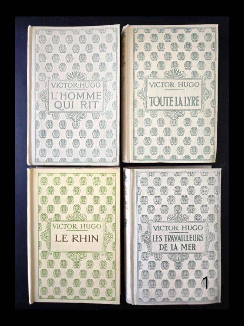 May include: Four vintage books by Victor Hugo. Each book has a cream-coloured cover with a repeating pattern of small, stylised floral designs. The titles include "L'Homme Qui Rit", "Toute La Lyre", "Le Rhin", and "Les Travailleurs De La Mer".