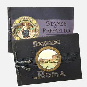 May include: Two rectangular black booklets bound with grey cord. The top booklet features a circular illustration of an angel and the text Stanze di Raffaello. The bottom booklet displays a circular image of a cityscape and the text Ricordo di Roma.