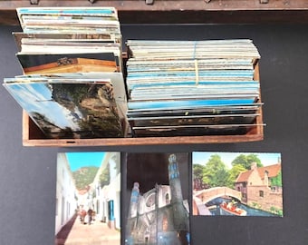 May include: A selection of vintage postcards depicting landscapes and buildings. The postcards are stored in a wooden rack, with several stacks of cards. A few individual postcards are arranged below the rack.