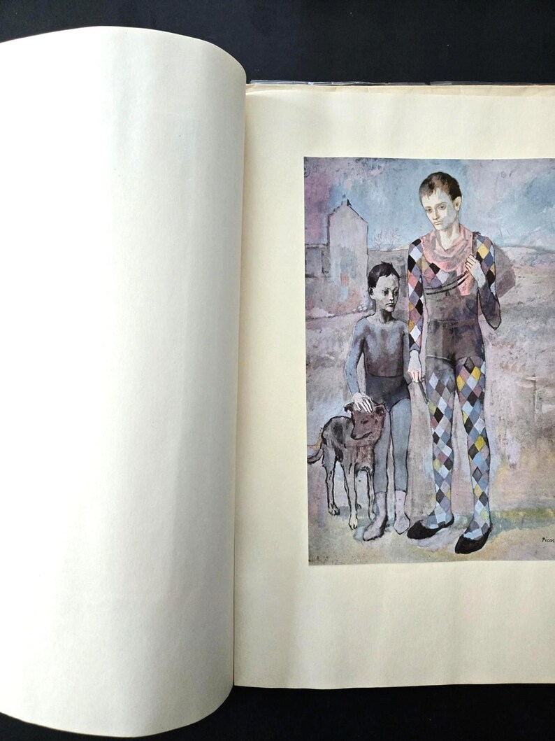 May include: A book page featuring a reproduction of a painting showing two figures and a dog. One figure wears a colorful diamond-patterned harlequin costume, while the other wears a dark grey outfit. The background is a muted landscape.