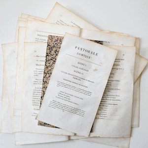 May include: A pile of old paper pages with text, including the title "PASTORALE COMIQUE". The pages are off-white with signs of age and some have decorative marbled paper. The text is in black ink.