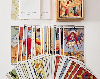 Op de afbeelding: Een vintage Tarot-deck met de titel "Le Tarot de Marseille" op de doos en het boekje. Het deck bevat kleurrijke illustraties op de kaarten, met een waaier van kaarten. De doos heeft een schilderij van een man aan een tafel.