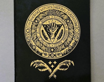 Op de afbeelding: Een zwart boek getiteld The Hedge Witch's Herbal Grimoire met goudfolie op de kaft. Het ontwerp bevat een cirkelvormig embleem met een hand, veren en tekst, plus twee gekruiste vogelklauwen en drie kleine sterren onder de cirkel.