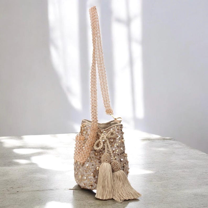 Handmade Wayuu crossbody bucket bag in beige, decorated with shimmering sequins, pearls, and tassels. The long beaded strap allows it to be worn comfortably on the shoulder or crossbody, while the artisan crochet base ensures durability and unique character. A versatile beaded bag perfect for special occasions, gifting, or adding a touch of luxury to everyday outfits.
