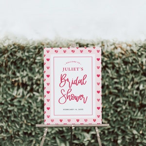 K&ouml;nnte beinhalten: Ein rosa-wei&szlig;es Schild f&uuml;r eine Brautparty mit einem Herzmuster als Rand. Auf dem Schild steht "Willkommen zur Brautparty von Juliet, 14. Februar 20XX".