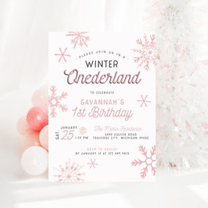 Op de afbeelding: Een roze en witte uitnodiging voor een 1e verjaardag met een winterwonderland thema. De uitnodiging bevat sneeuwvlokken en de tekst "PLEASE JOIN US IN A WINTER ONEDERLAND TO CELEBRATE SAVANNAH'S 1st BIRTHDAY". De uitnodiging bevat ook de datum, tijd en locatie van het feest.