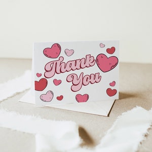 May include: A white card with the words "Thank You" in pink script surrounded by pink and red hearts.