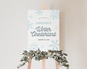 May include: A white sign with blue snowflakes and the text "Welcome to Christian's Winter Wonderland, January 25, 20XX" on an easel with greenery.