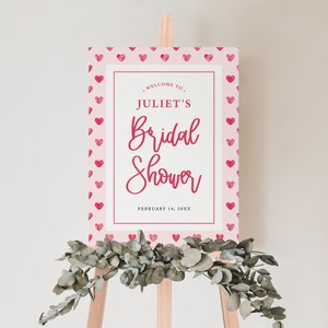 K&ouml;nnte beinhalten: Ein rosa-wei&szlig;es Schild mit rotem Herzrand und dem Text "Willkommen zu Juliets Bridal Shower, 14. Februar 20XX".